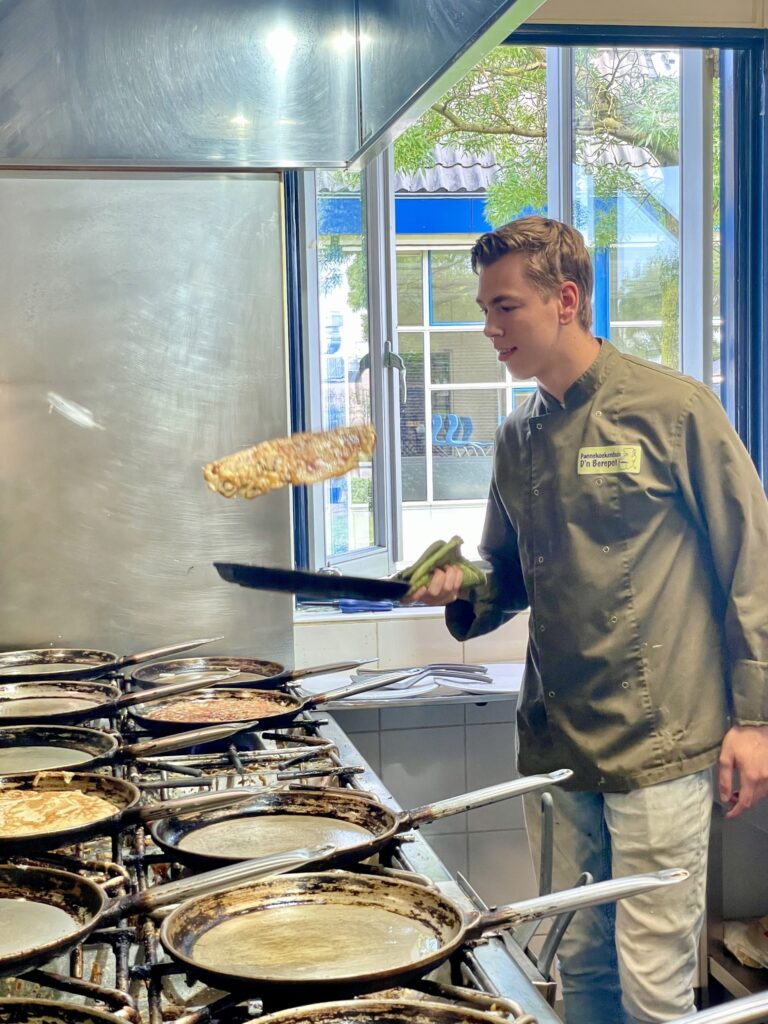 Een personeelslid van D'n Berepot flipt een pannenkoek in de pan